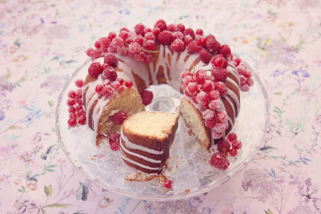 Slice of lemon drizzle bundt cake, decorated with sugared raspberries and redcurrants
