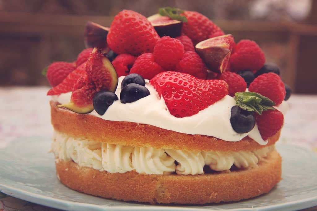 A victoria sponge topped with fresh cream and a variety of fruit
