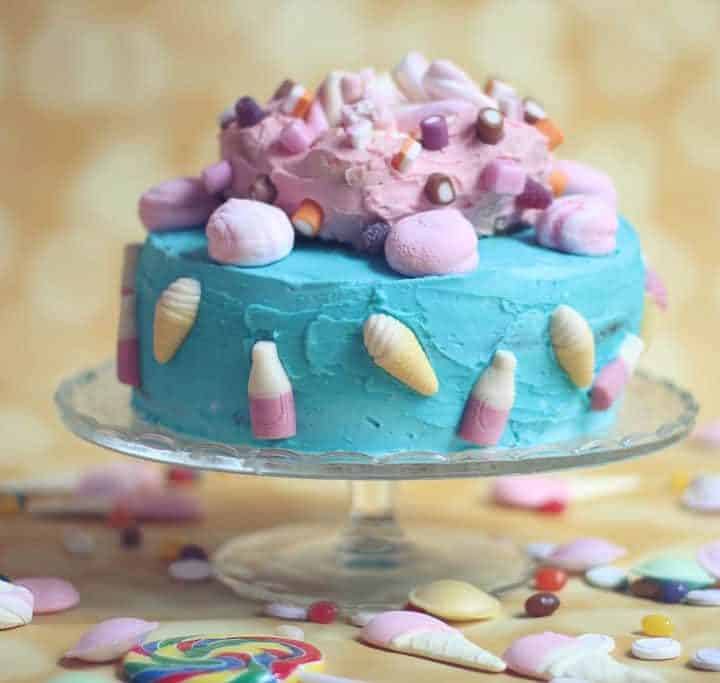 Sponge cake covered with bright blue inning and a pink iced ring on top covered in sweets. Child’s birthday cake.