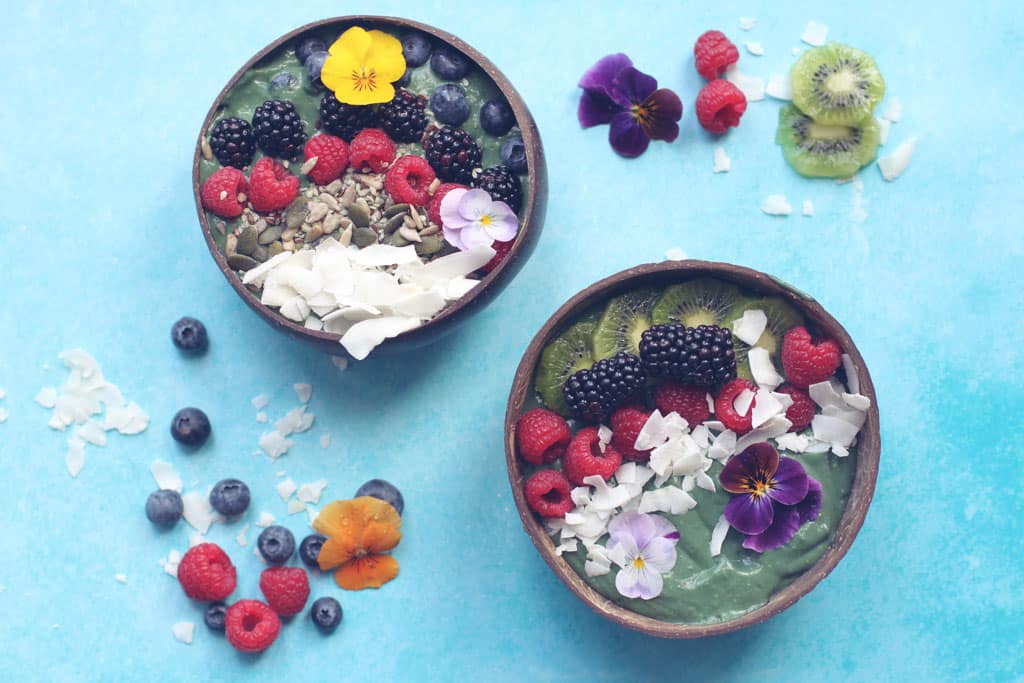 Two green smoothie bowls made with spirulina and topped with fresh fruit