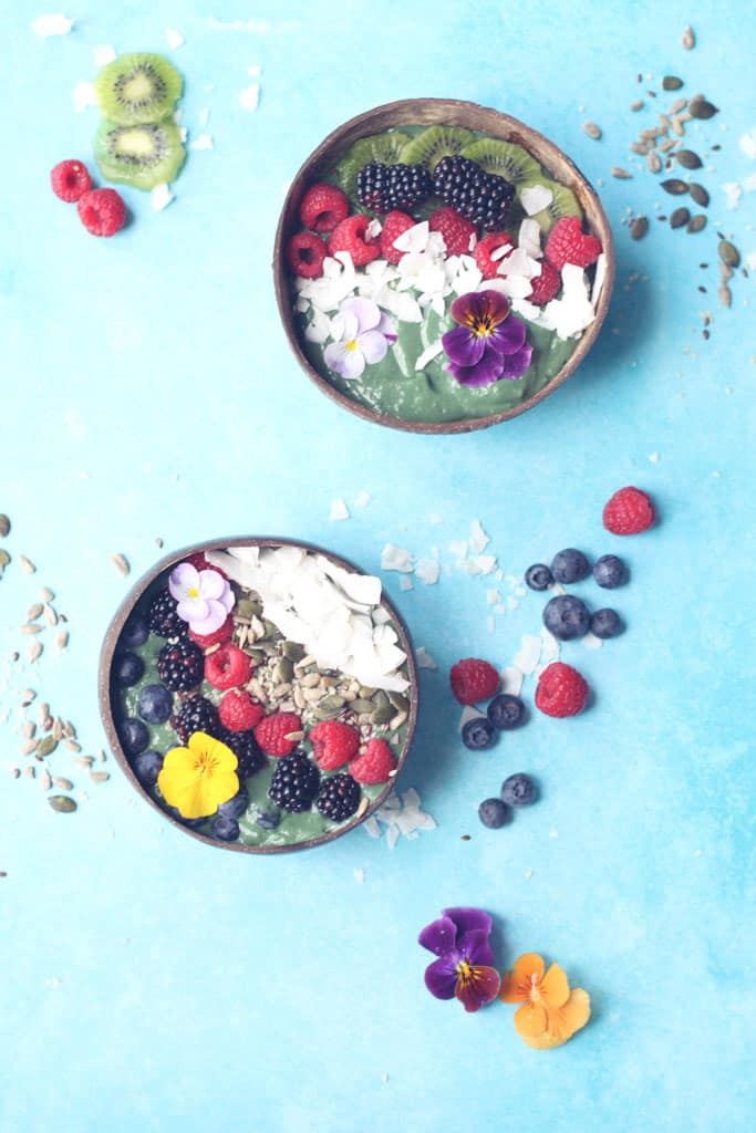 Overhead shot of two green smoothie bowls topped with fresh fruit