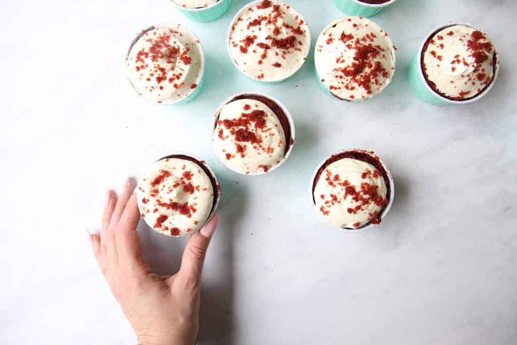 Hand reaching out to take a red velvet cupcake