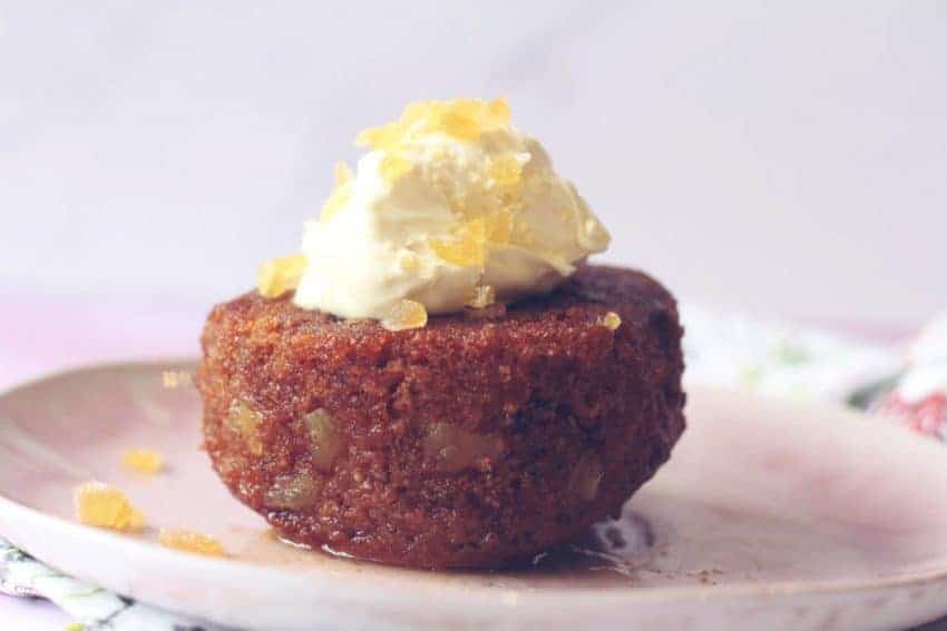 Side view of an individual sticky ginger cake topped with clotted cream and crystallised ginger