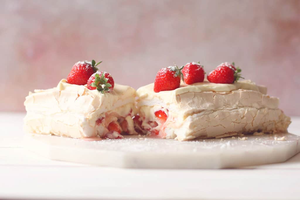 An Eton Mess Roulade cut in half with strawberries on top and a cream and yoghurt filling
