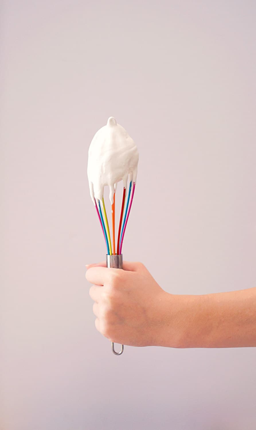 A hand holding a whisk covered in buttercream icing.