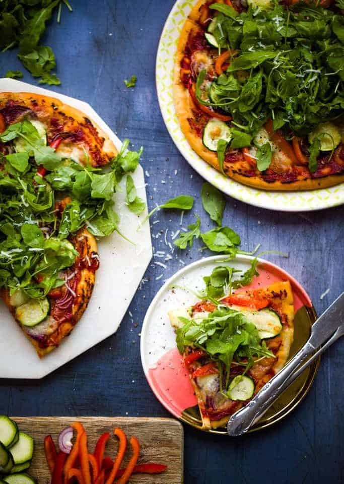 Overhead shot of vegetable pizza on a chopping board beside a plate with a slice of pizza