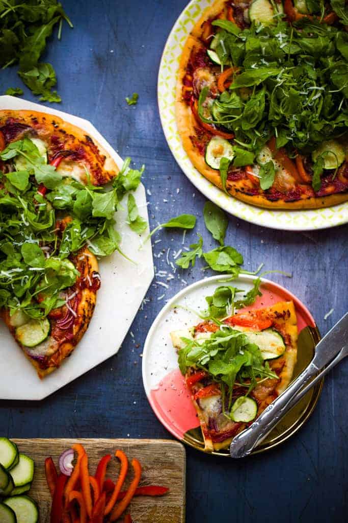 Overhead shot of vegetable pizza on a chopping board beside a plate with a slice of pizza