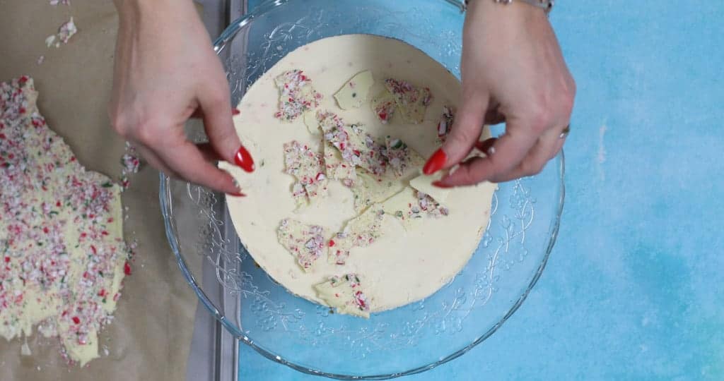 Decorating the top of a peppemint bark cheesecake with shards of peppermint bark