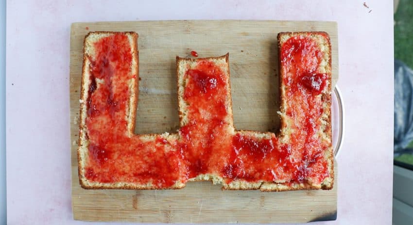 spreading strawberry jam onto a letter cake