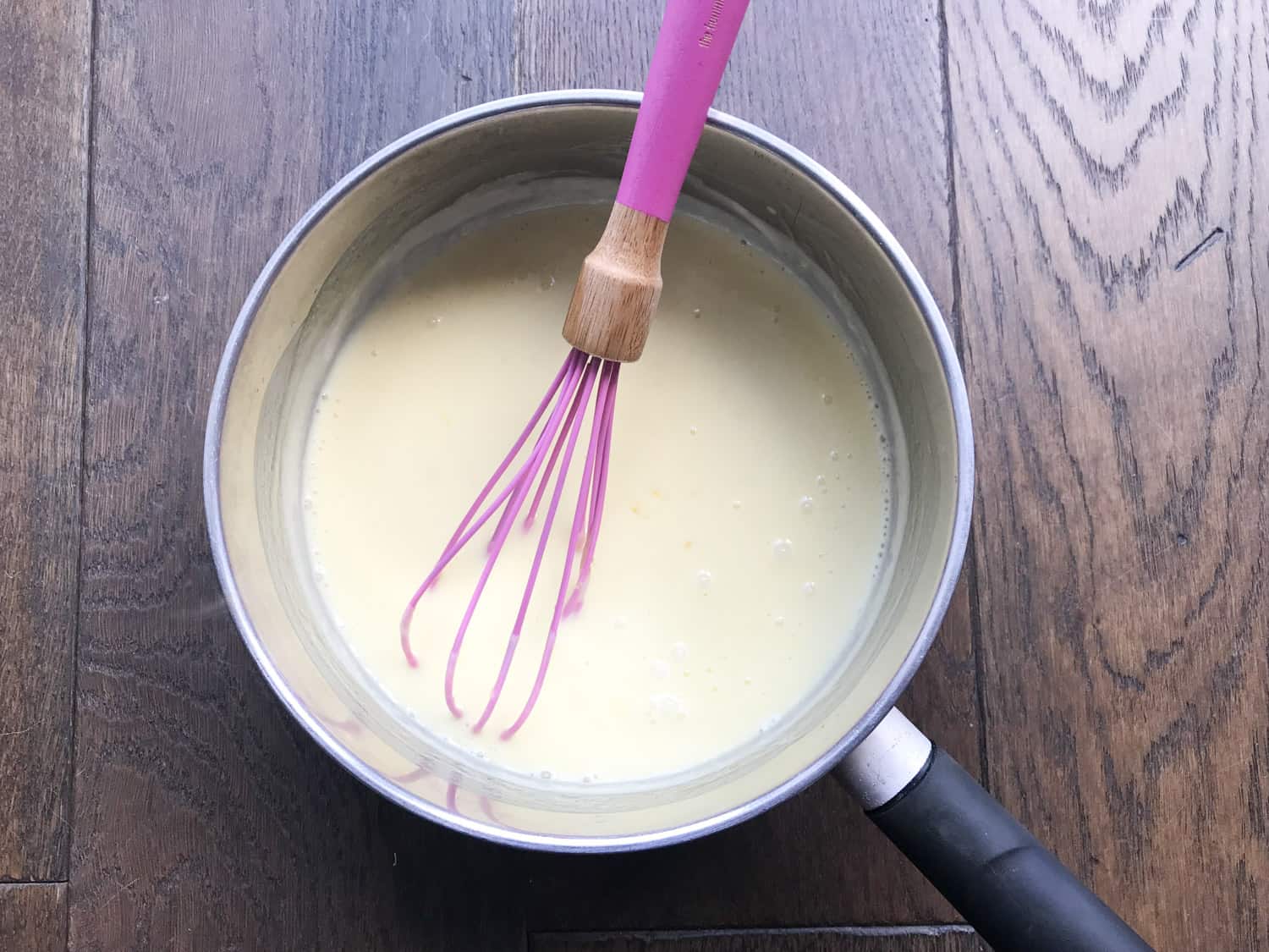 A saucepan with cream, sugar, lemon zest and lemon juice with a whisk inside