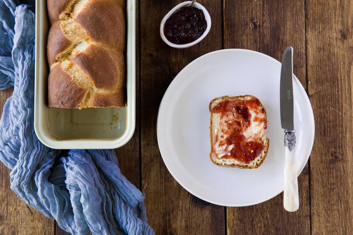 A loaf od brioche bread with a slice cut from it covered with butter and jam