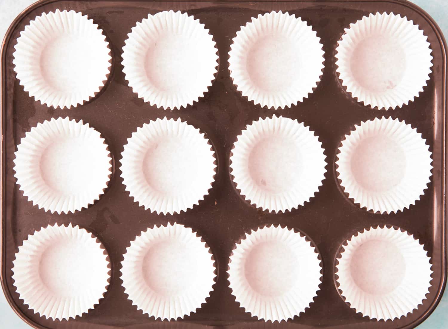 A 12 hole cupcake tray lined with 12 white cupcake cases