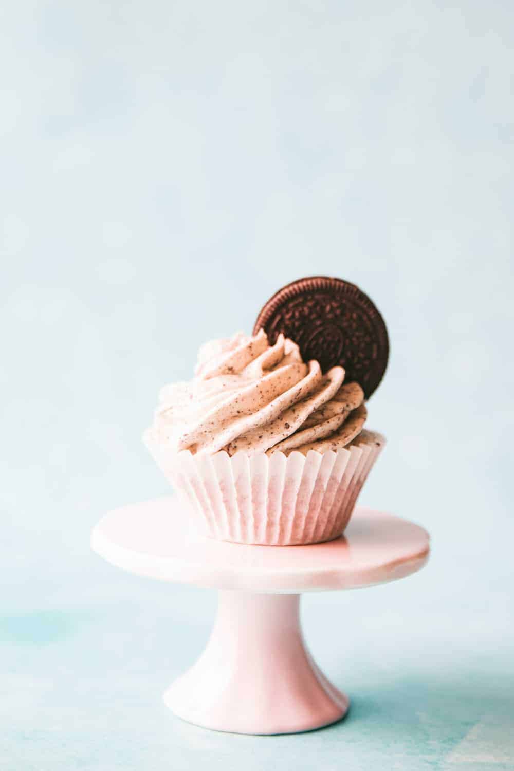 An Oreo cupcake on top of a small pink cupcake stand 