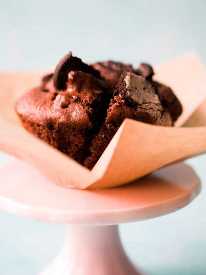 Side view of an Oreo muffin in a brown muffin case on top of a small pink cake stand