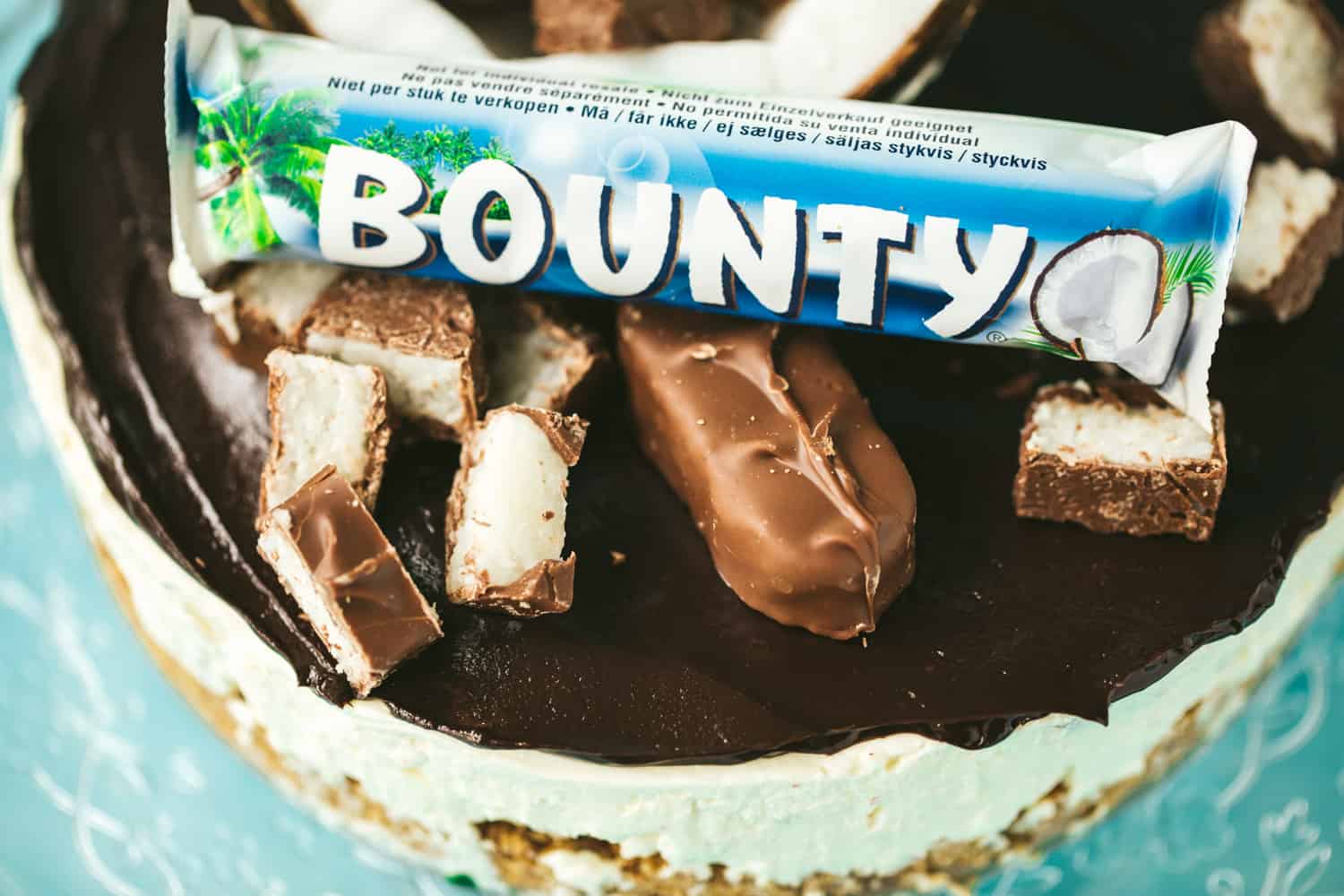 A cheesecake with chocolate ganache on top, half a coconut and Bounty bars are decorating the cheesecake