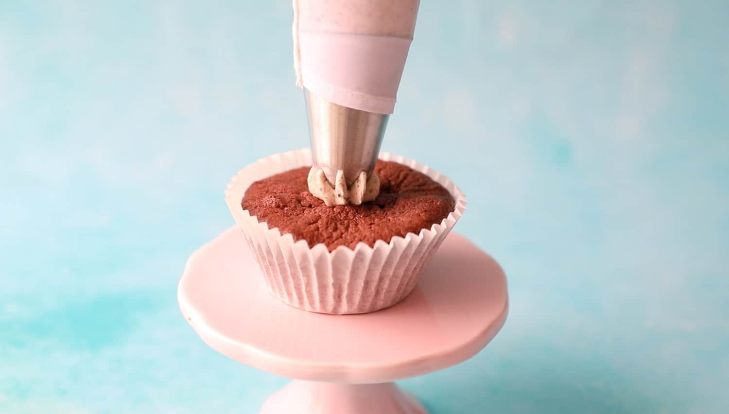 A cupcake on a pink stand about to be iced