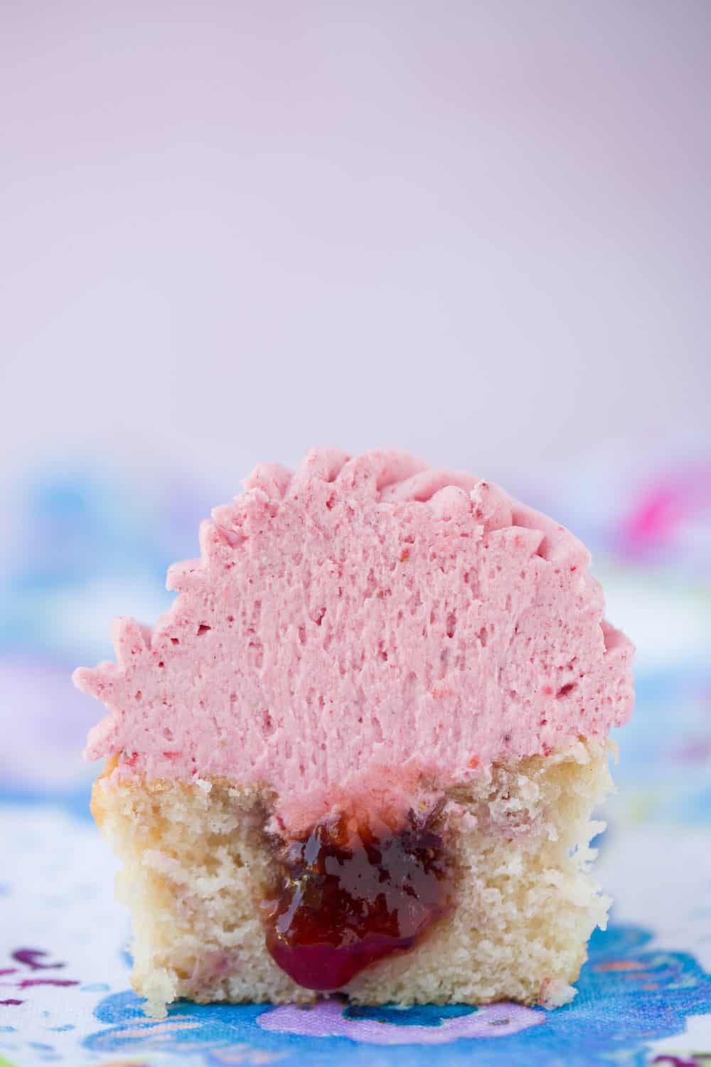A strawberry cupcake cut in half to show the jelly filling in the centre