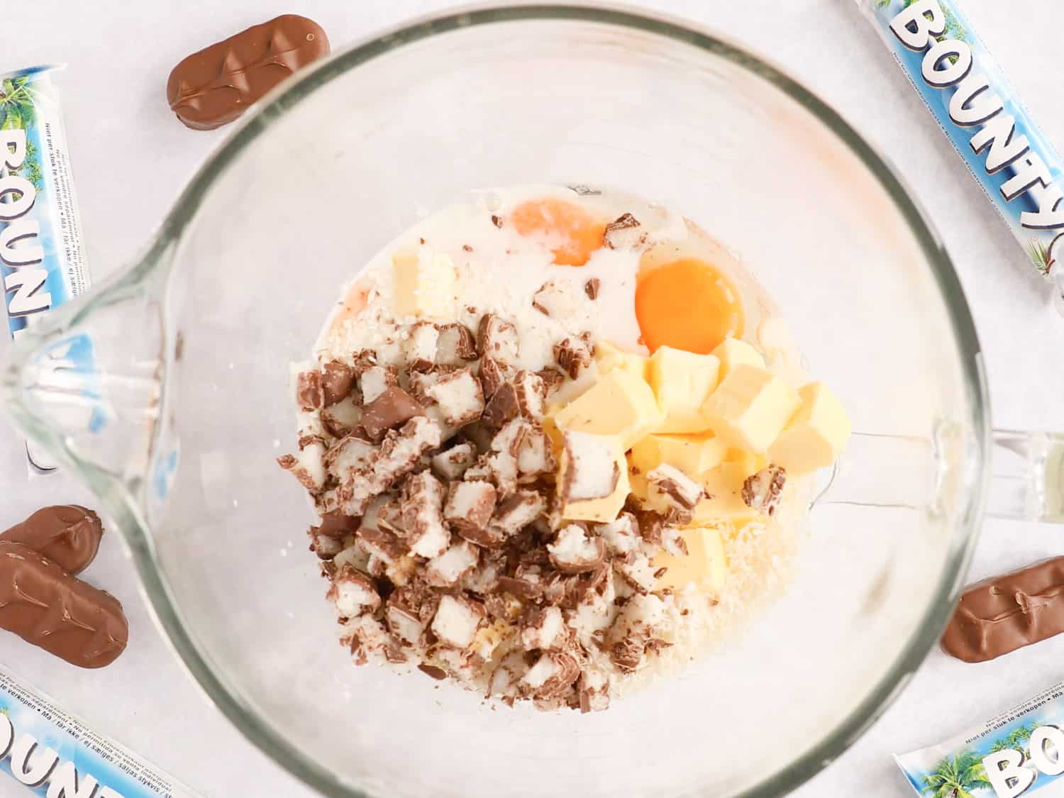 A mixing bowl with butter, sugar, eggs, flour and chopped Bounty bars