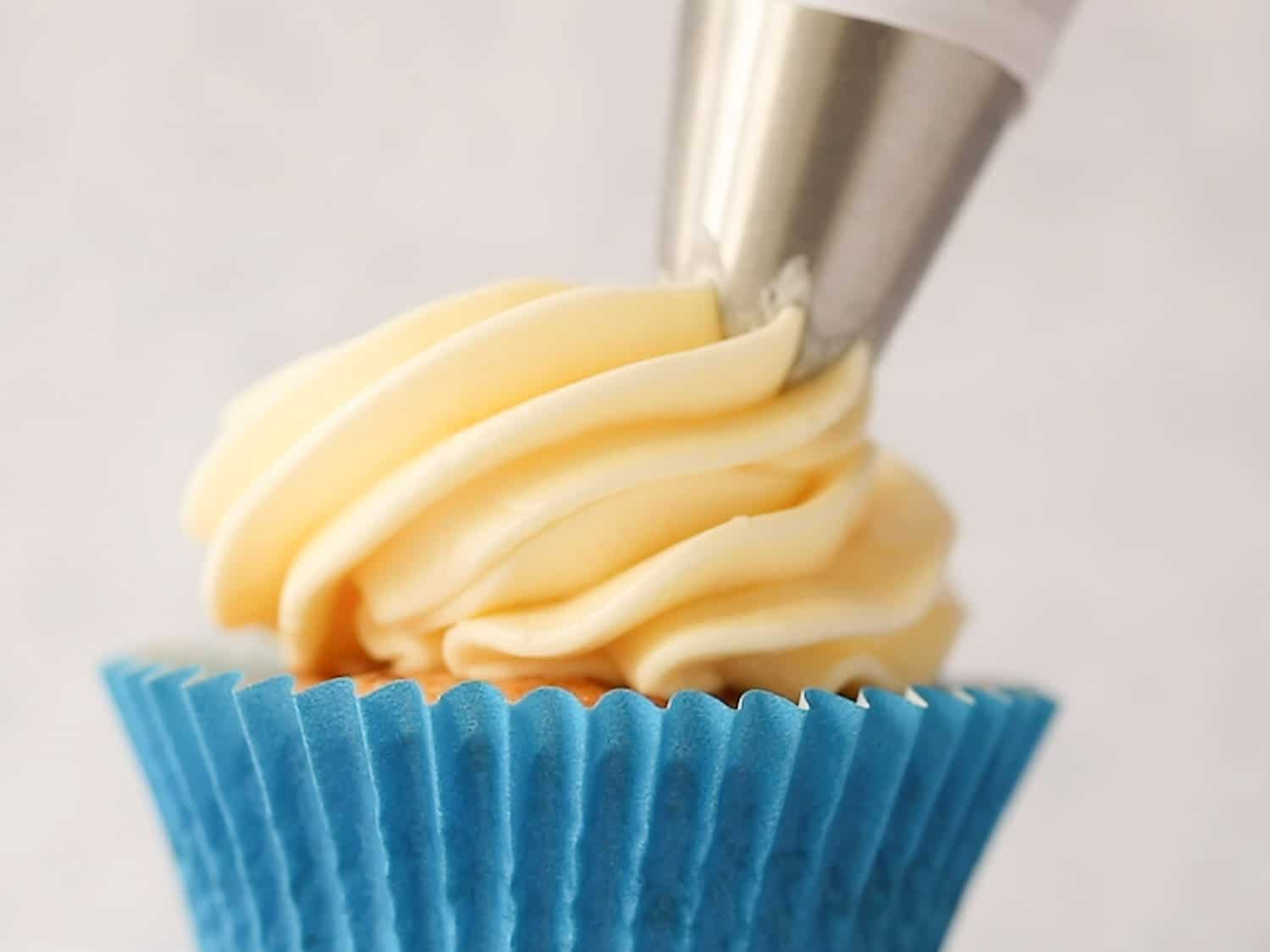 A cupcake in a blue case being decorated with buttercream