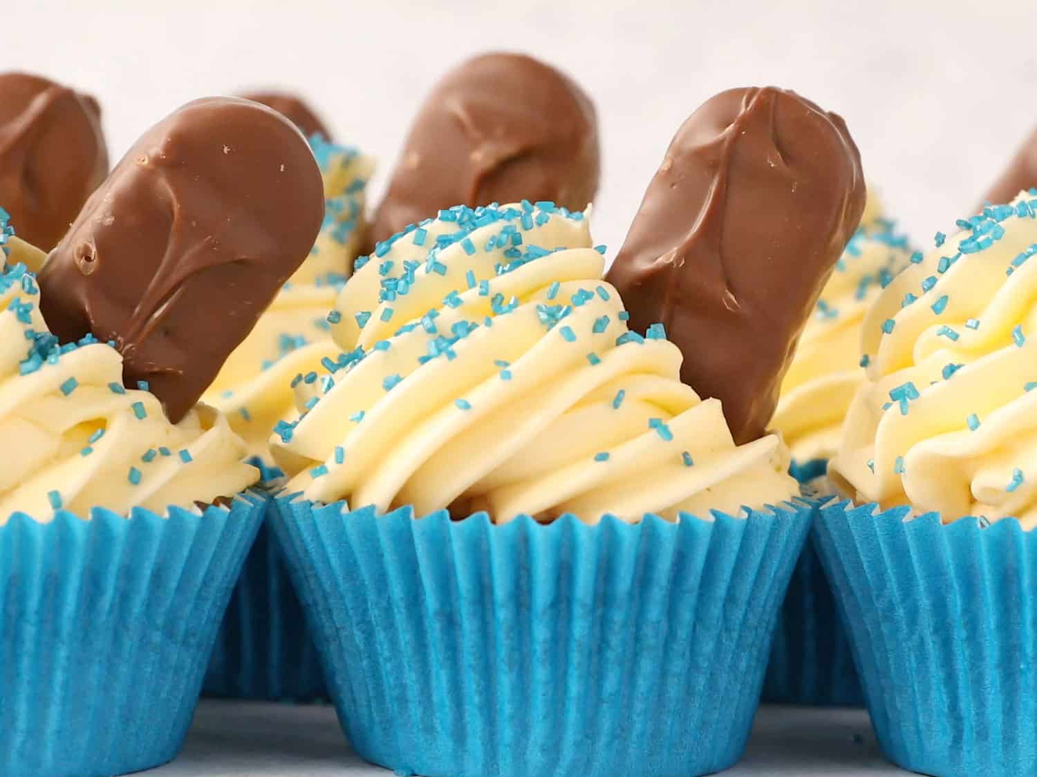 A row of cupcakes in blue cupcake cases, the cupcakes have been decorated with buttercream and a Bounty bar