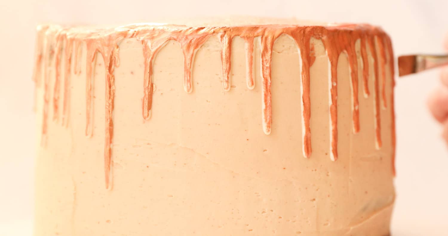 Close up of a chocolate layer cake that has been covered in Nutella buttercream, the cake has white chocolate dripping down its sides and is being painted with gold food paint