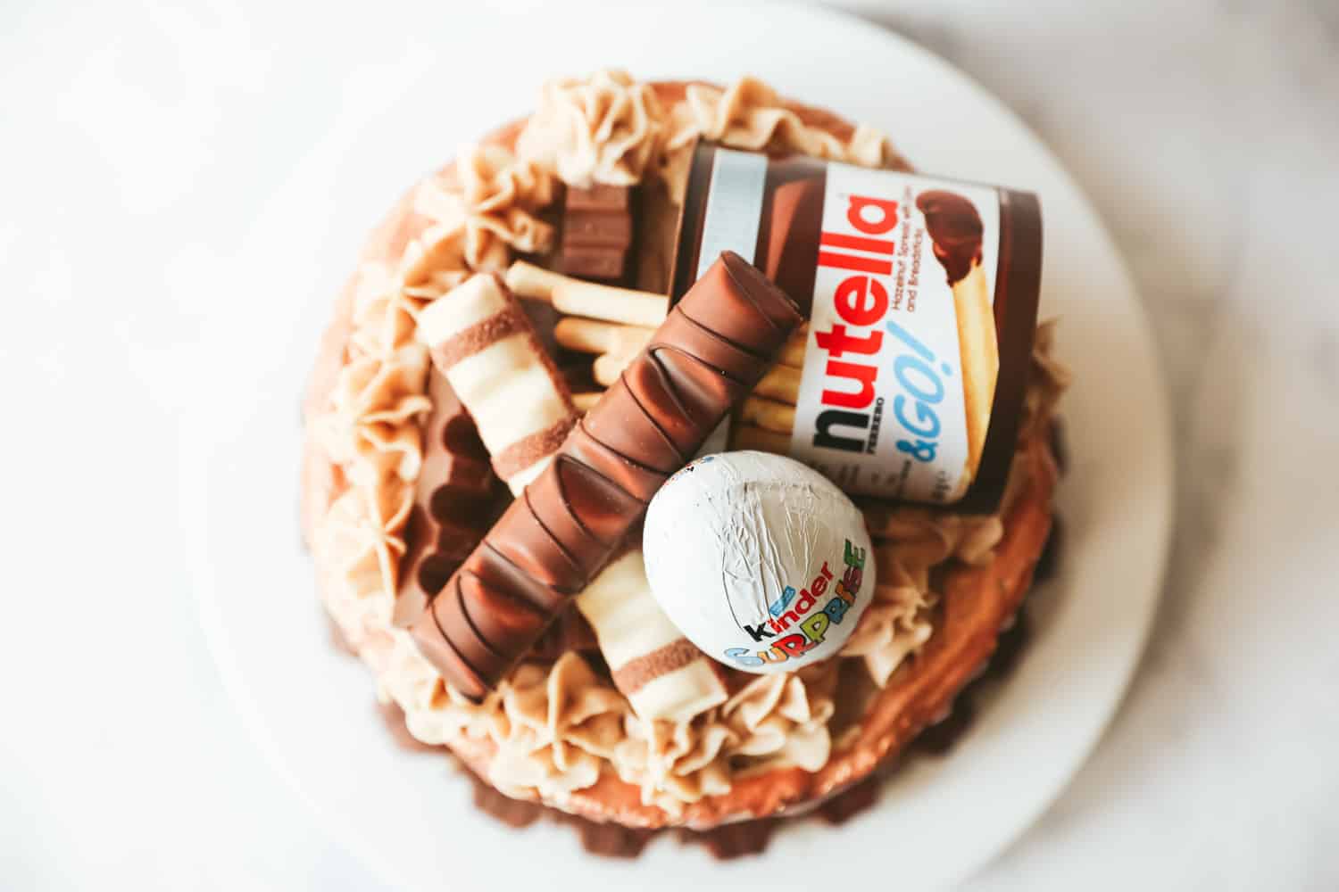 Overhead view of a Kinder cake decorated with a Nutella and Go, a Kinder Egg, Kinder chocolate and Kinder Bueno