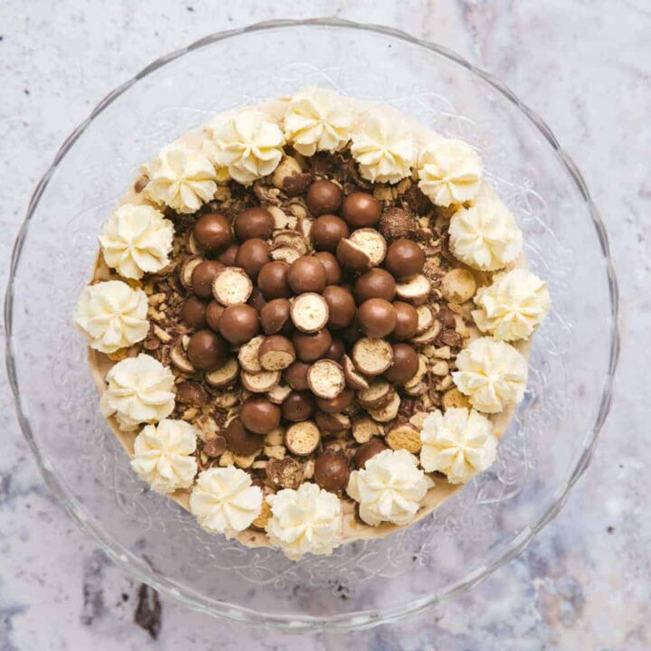 Overhead view of a Malteser cheesecake on a glass cake stand