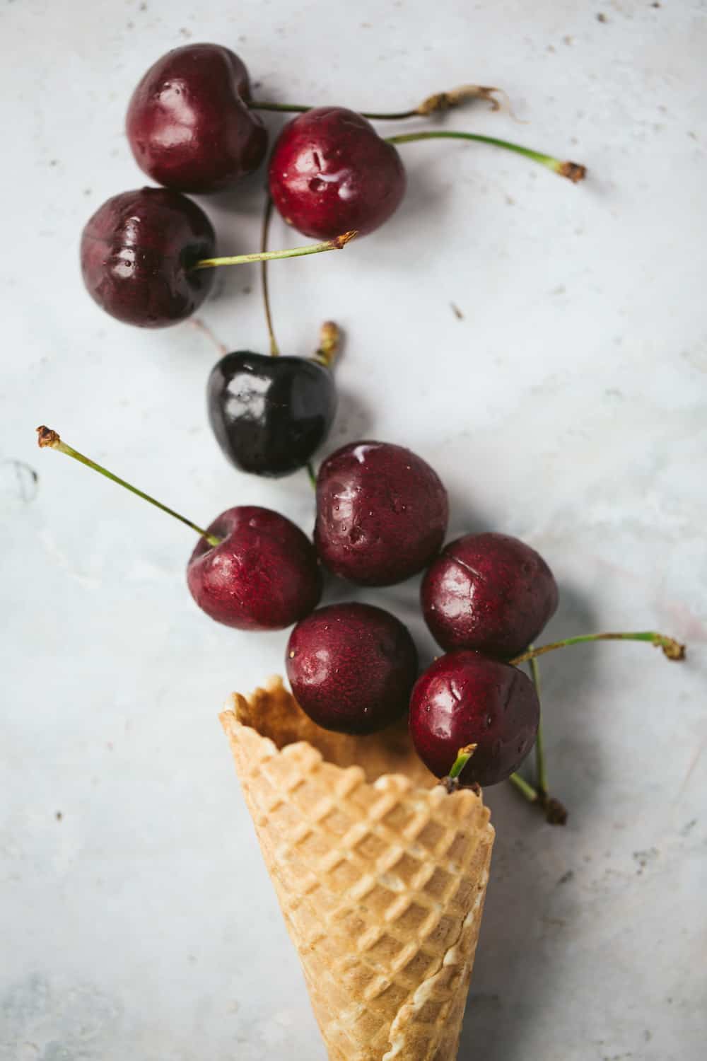 A waffle ice cream cone with fresh black cherries spilling out.
