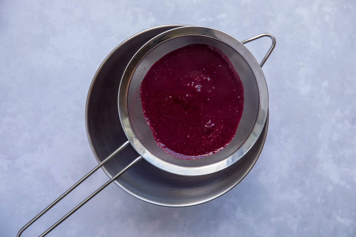 A saucepan with a sieve on top of it that contains black cherries being passed through the sieve. The saucepan is collecting the juice. 