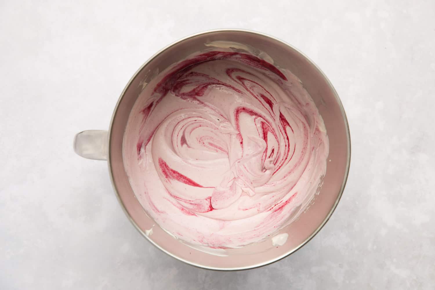 A mixing bowl containing black cherry ice cream mixture with swirls of black cherry sauce. 