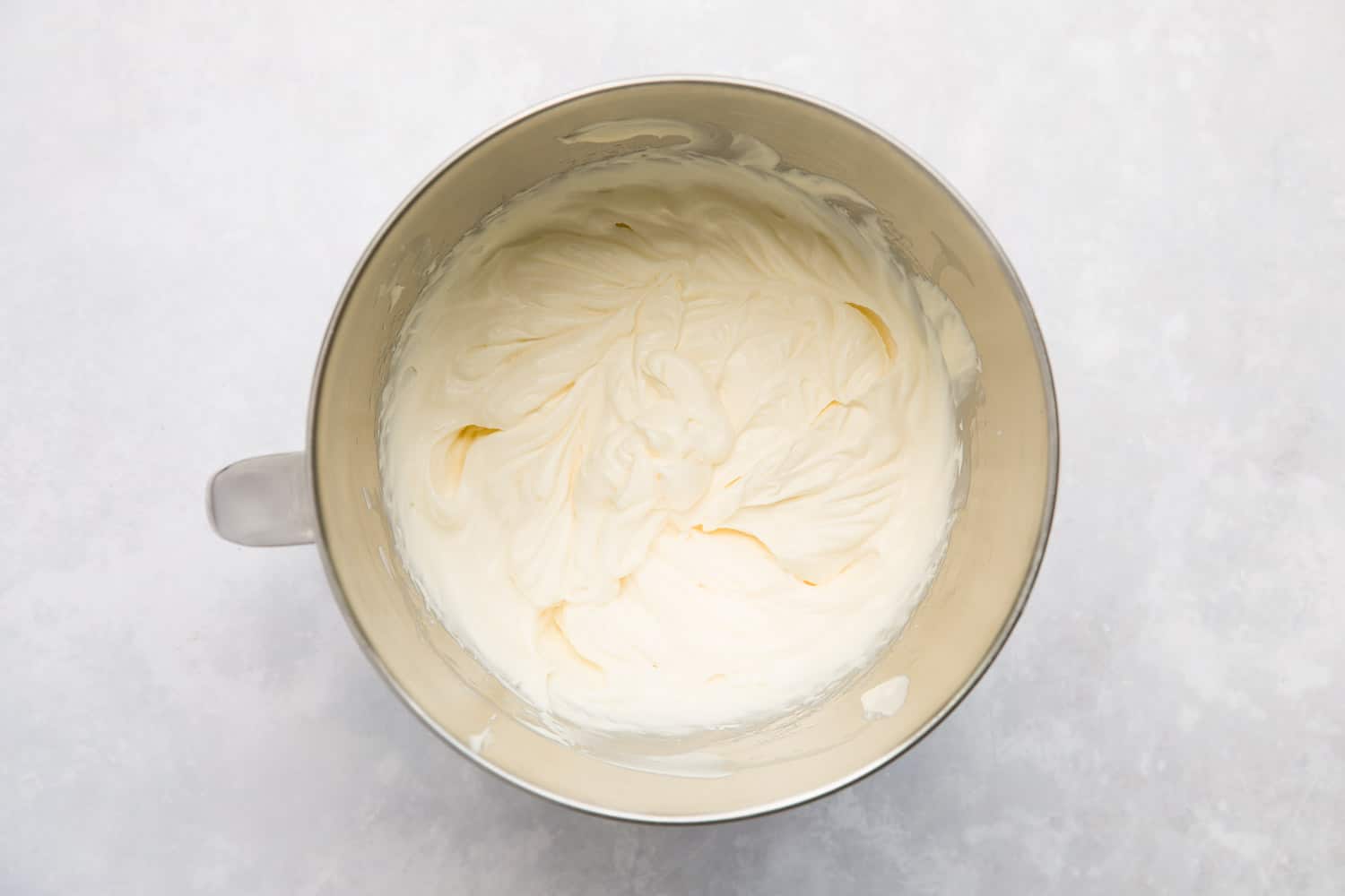A mixing bowl containing whipped double cream and condensed milk. 