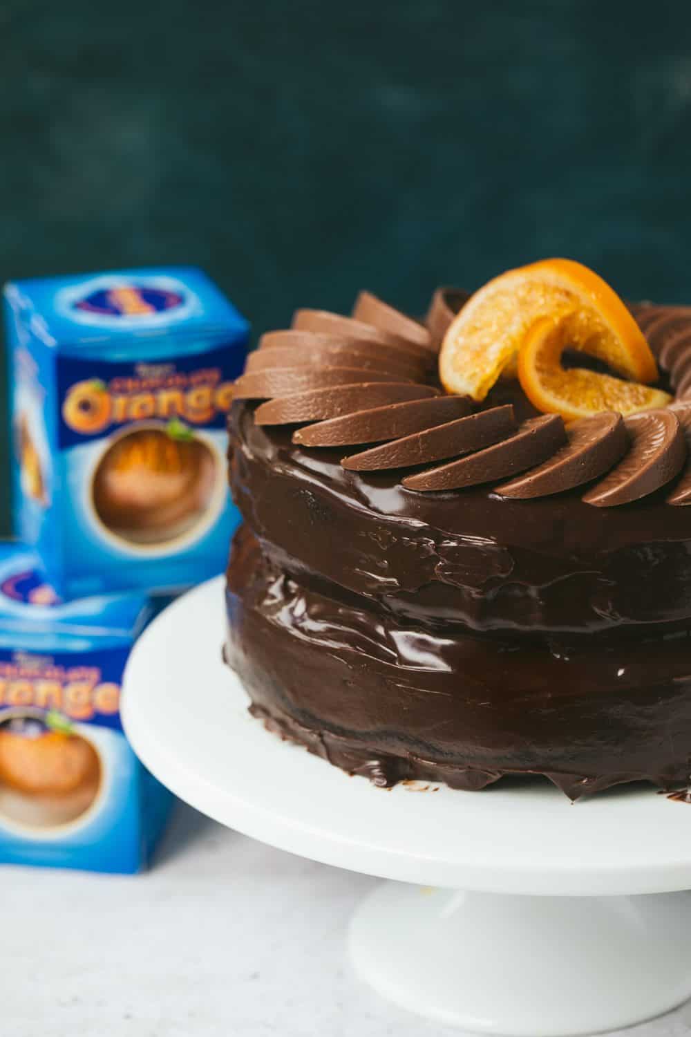 A chocolate orange cake topped with Terry's chocolate orange segments. There are 3 boxes of chocolate oranges visible in the background.