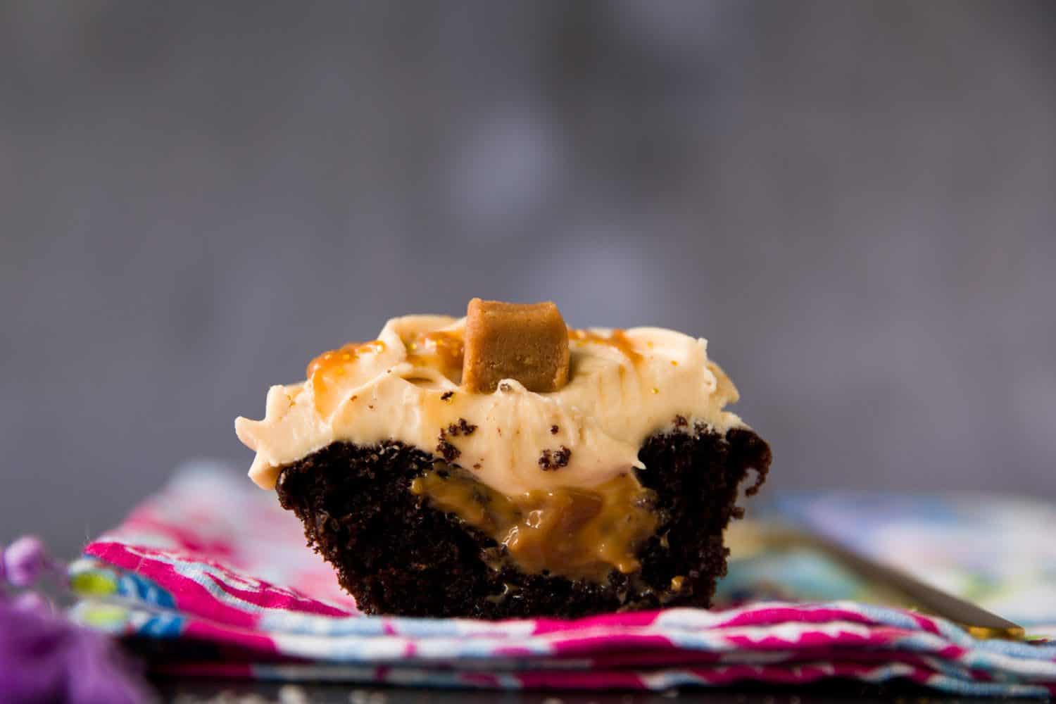 A chocolate cupcake that has been cut open. There is caramel sauce in the middle and a piece of fudge on top of the cupcake. 