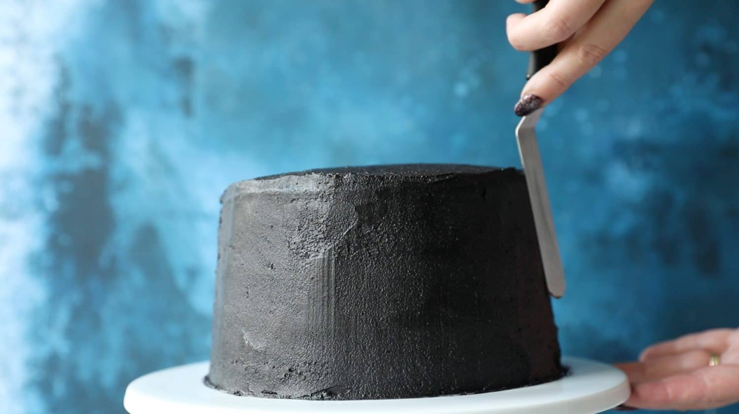 A tall cake that has been covered in black buttercream icing.