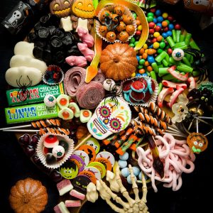 A Platter filled with Halloween sweets, candy and chocolate. There is a skeleton hand reaching in at the bottom of the platter.