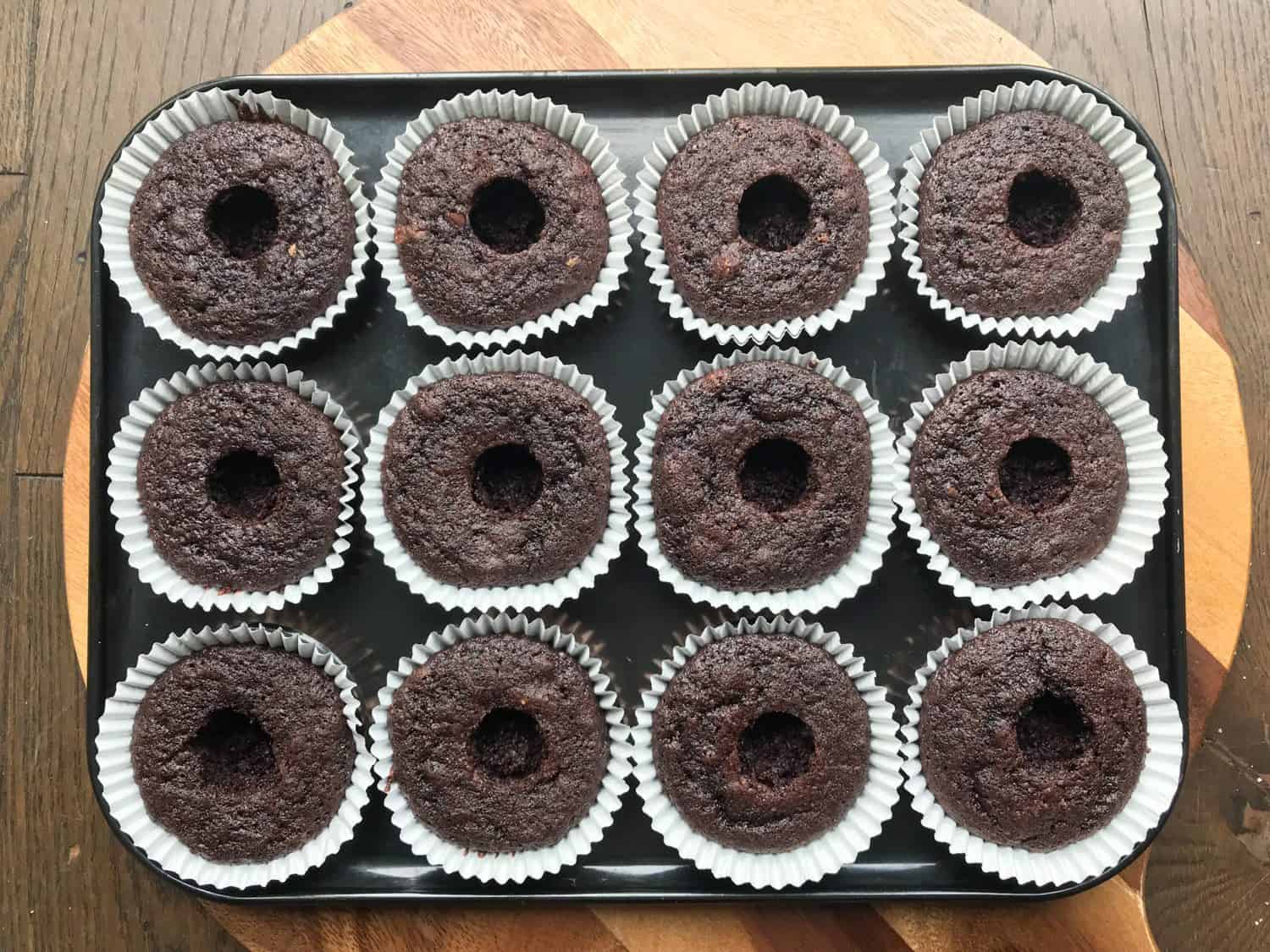 A tray of 12 chocolate cupcakes with holes in the centre. 