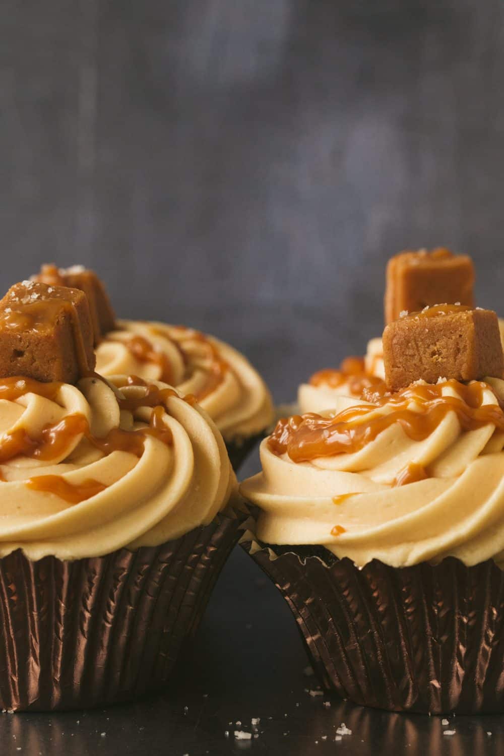 A group of four cupcakes each topped with frosting a piece of fudge and caramel sauce. 