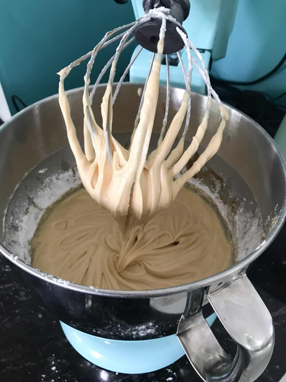 A Blue KitchenAid stand mixer fitted with the whisk attachment. In the bowl is salted caramel frosting. 