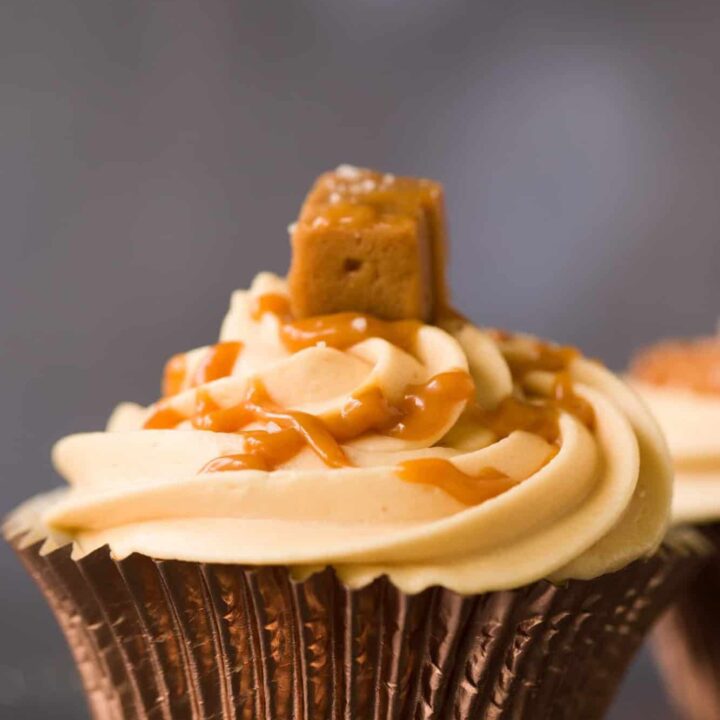Profile of a salted caramel cupcake in a rose gold cupcake case. There is icing on top of the cupcake and a piece of fudge.