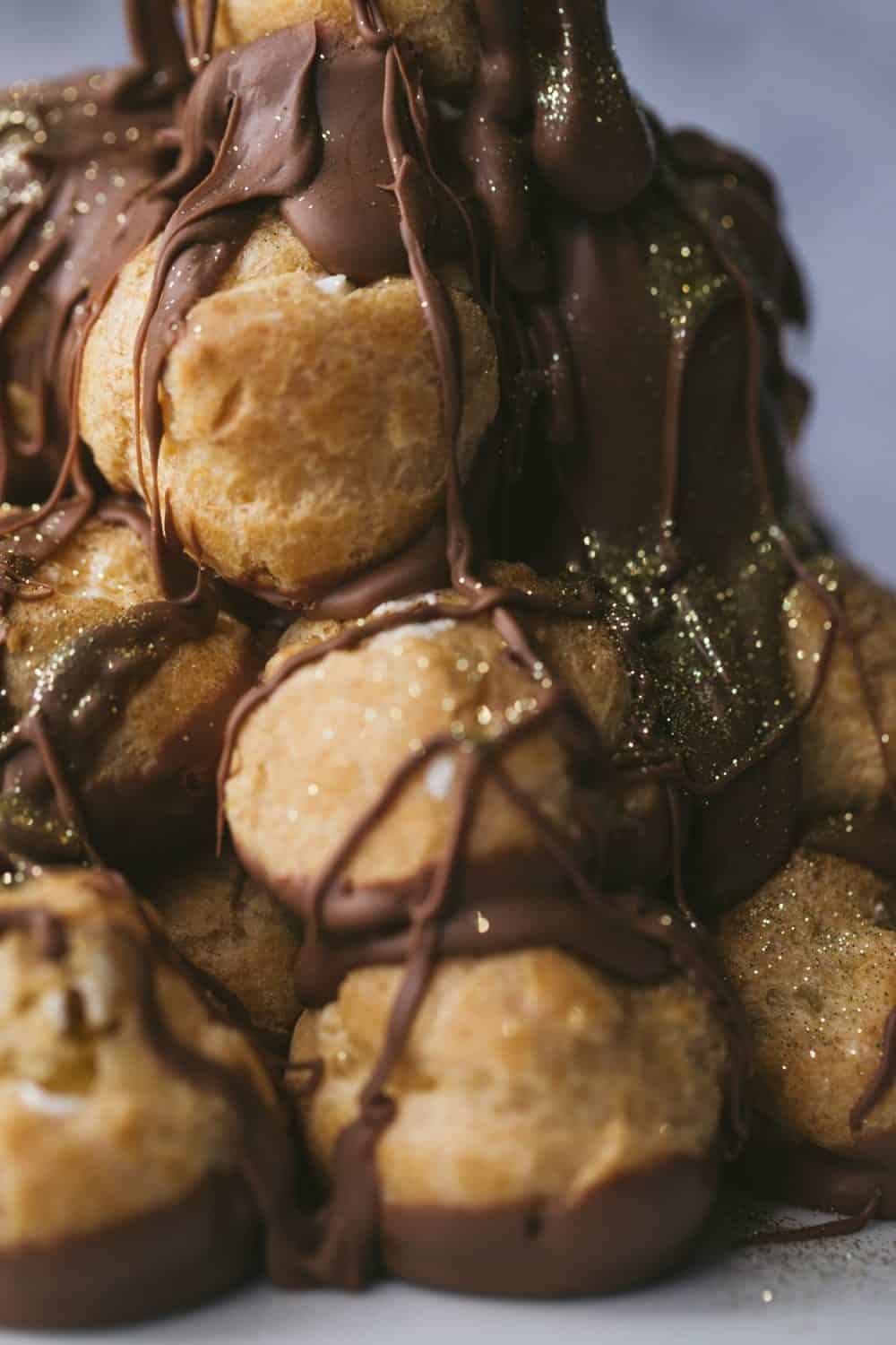 A close up image of profiteroles stacked and covered with chocolate sauce. 