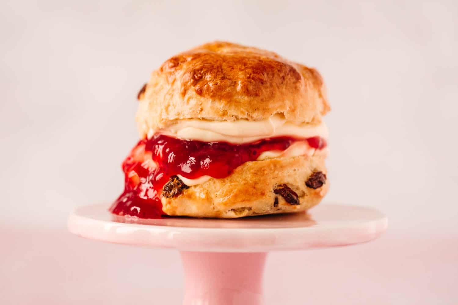 Profile image of a scone on a pink cake stand with a pale pink background. 
