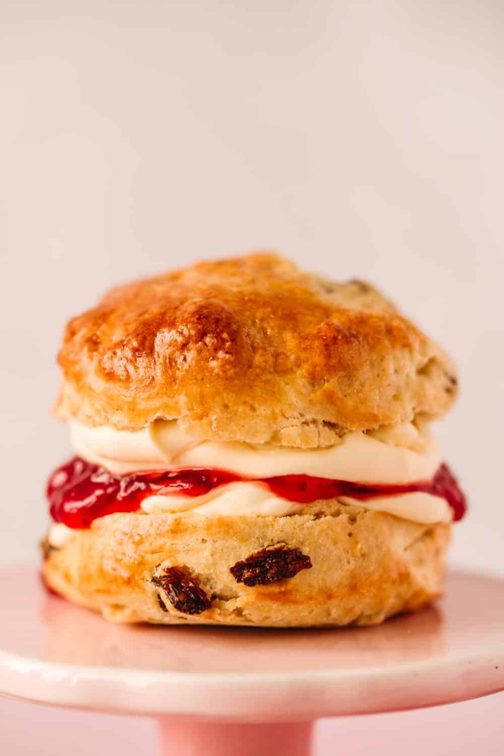 A fruit scone that has been cut in half and has strawberry jam and clotted cream spread on it. 