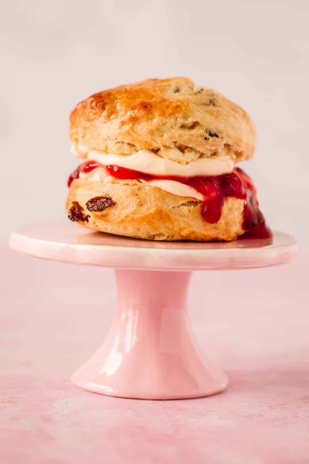 A fruit scone on a small pale pink cake stand. 