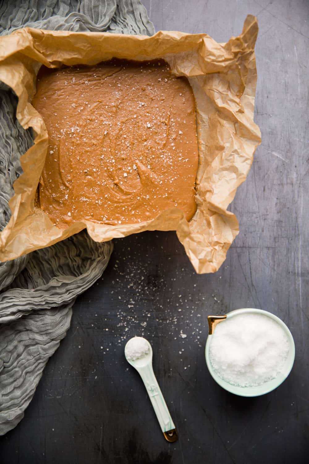 Creamy caramel fudge in a baking tin next to a pot containing sea salt. 