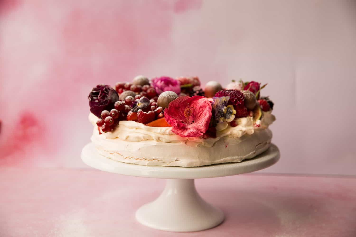 Pink background with a  pavlova dessert on a white cake stand.