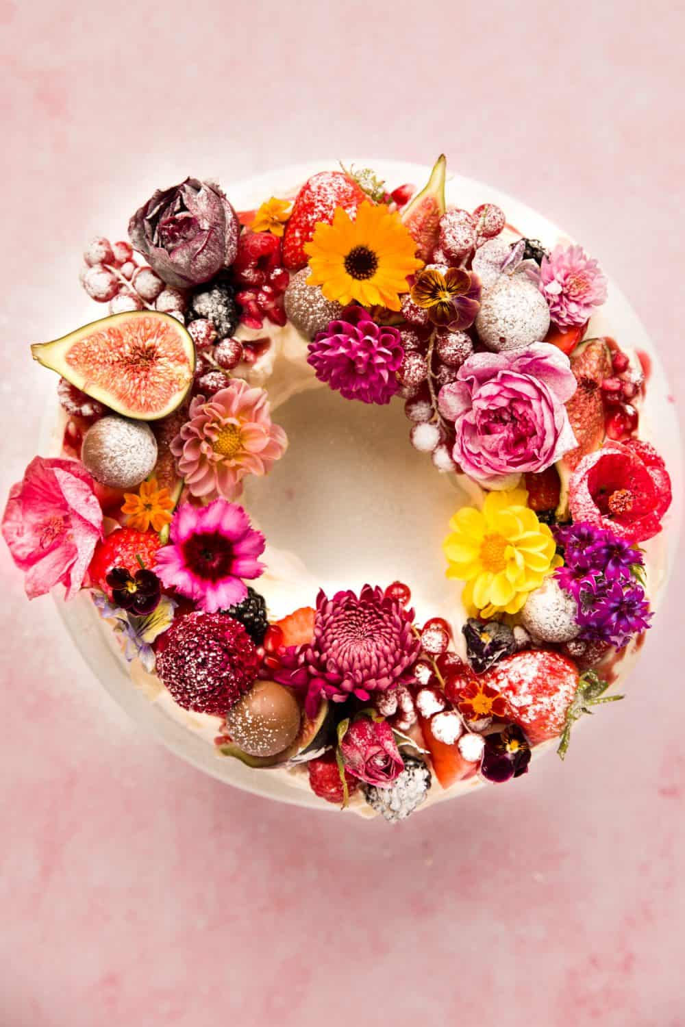 Overhead of a wreath shaped pavlova covered in fruit ad edible flowers. 