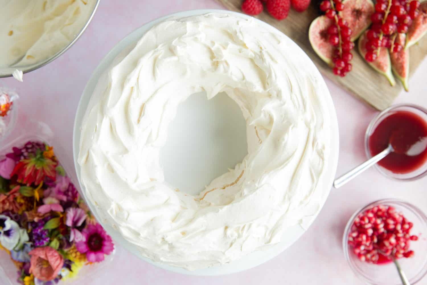 A meringue wreath on a white cake stand that has had double cream spread on to the top. 