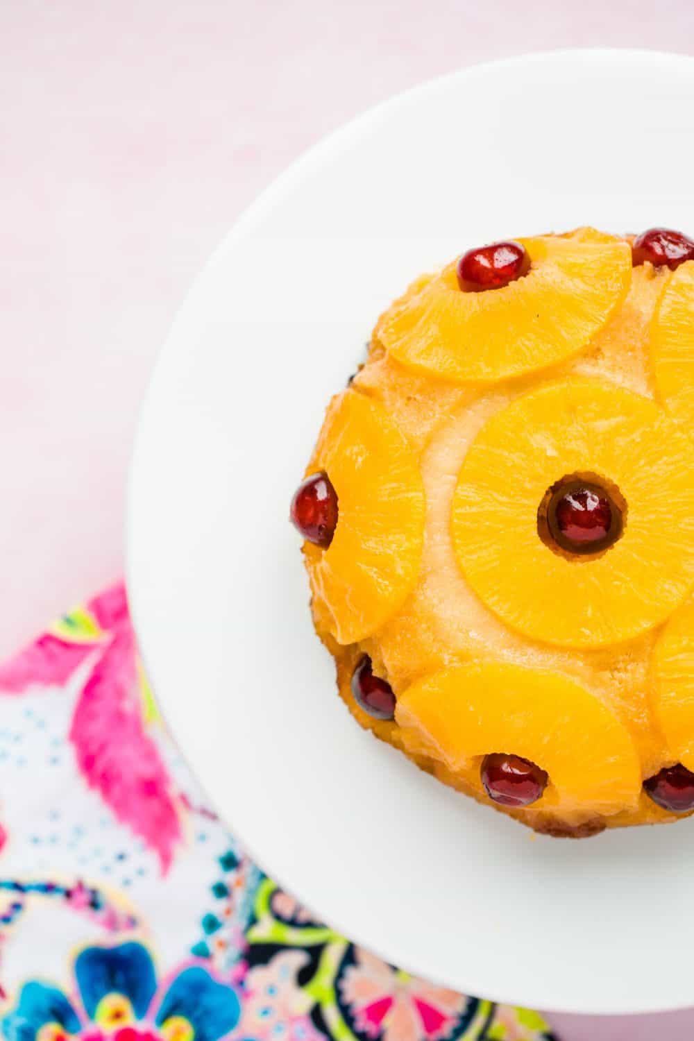 A steamed cake covered in pineapple rings and glace cherries on a large white serving plate. 