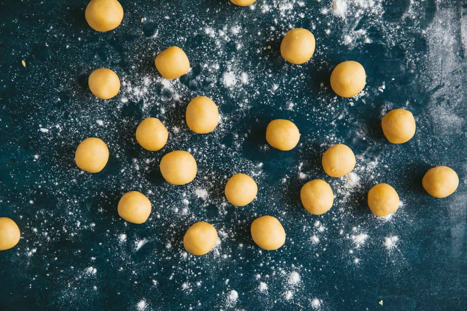 Balls of biscuit dough on a dark green surface. 
