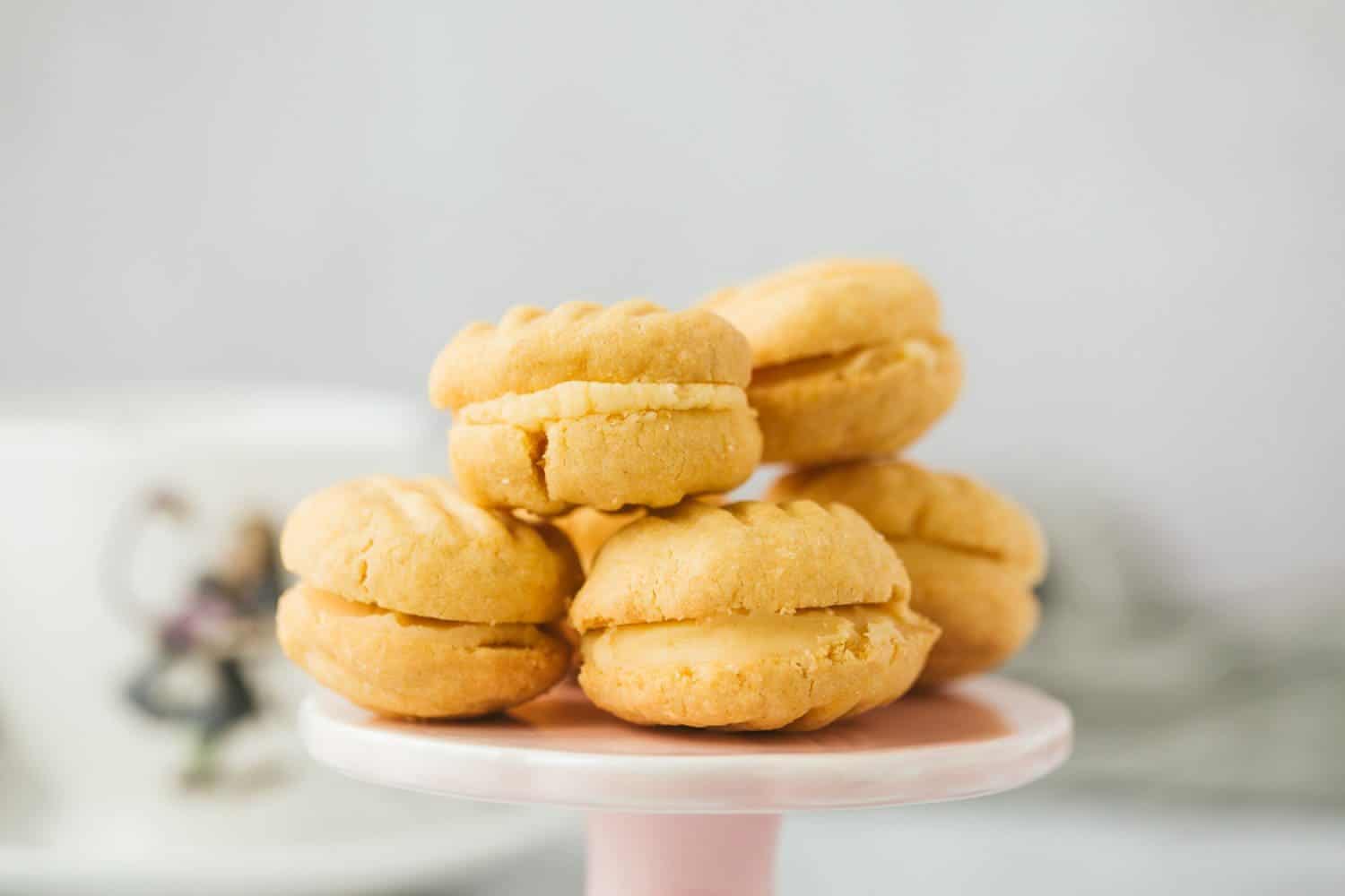 A pile of pale yellow custard cream cookies on a pink stand. 
